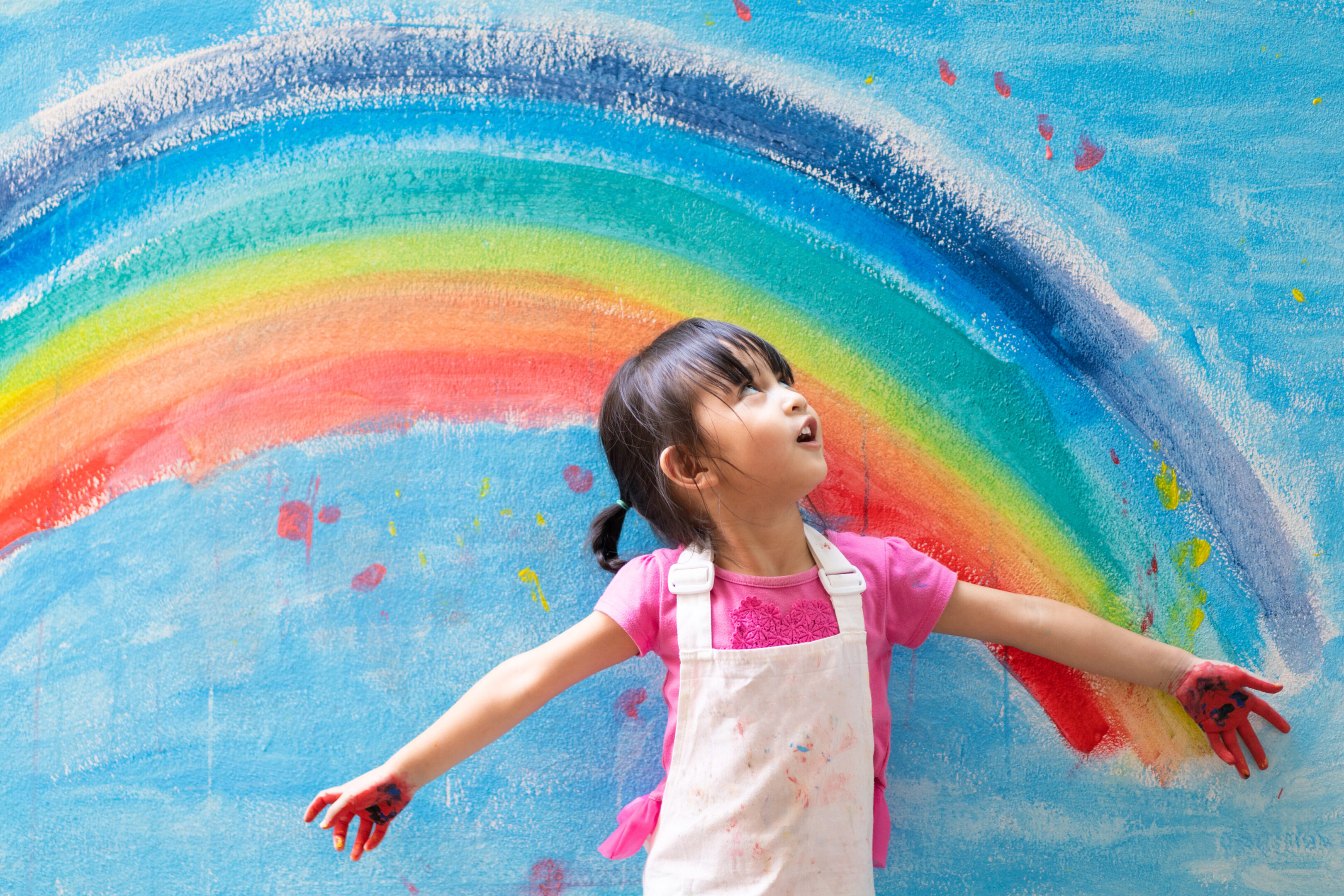 Asian little girl is painting the colorful rainbow and sky on th